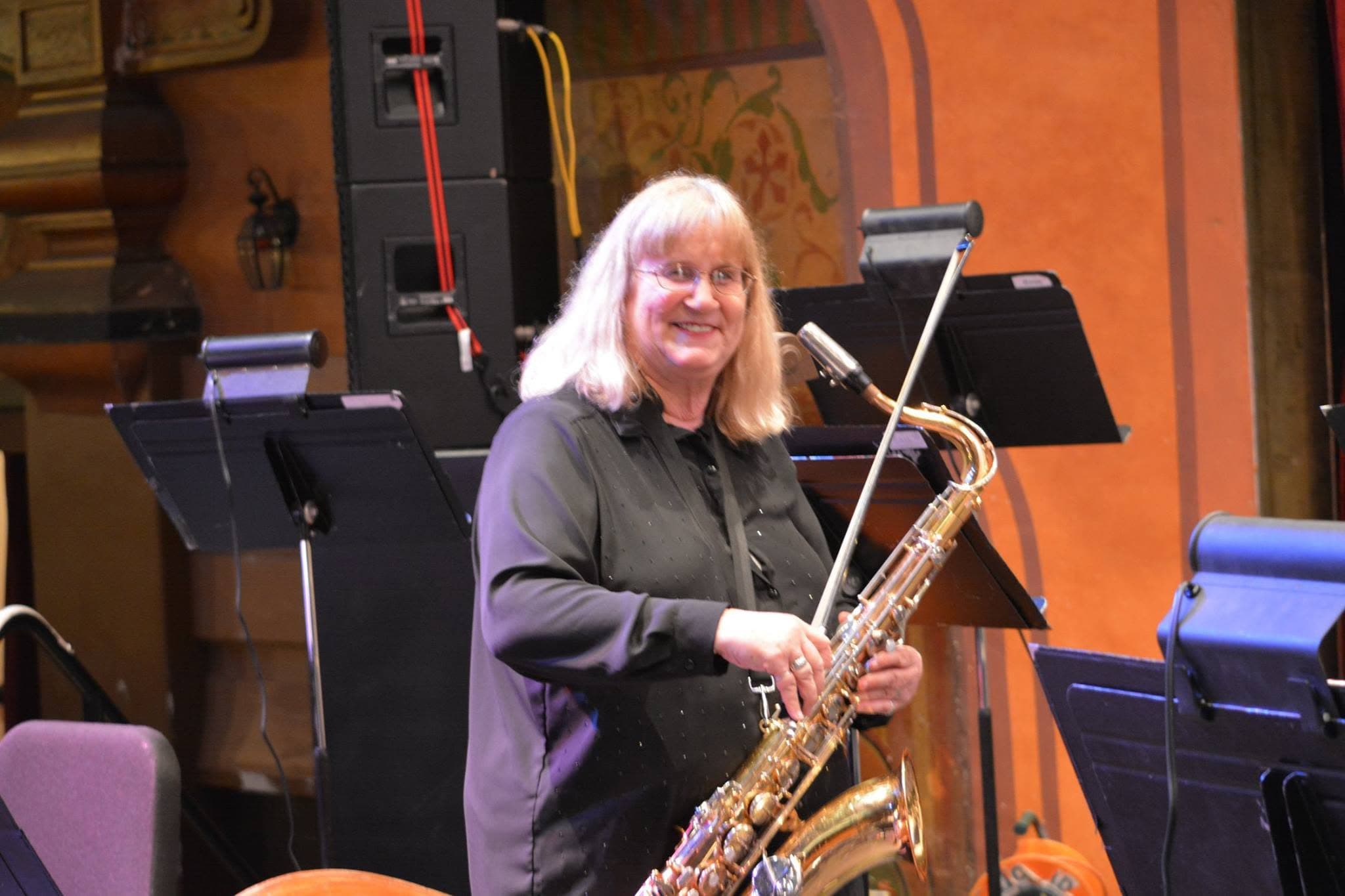 Dr. Colleen Snyder on stage with a baritone saxophone, music stands around her.