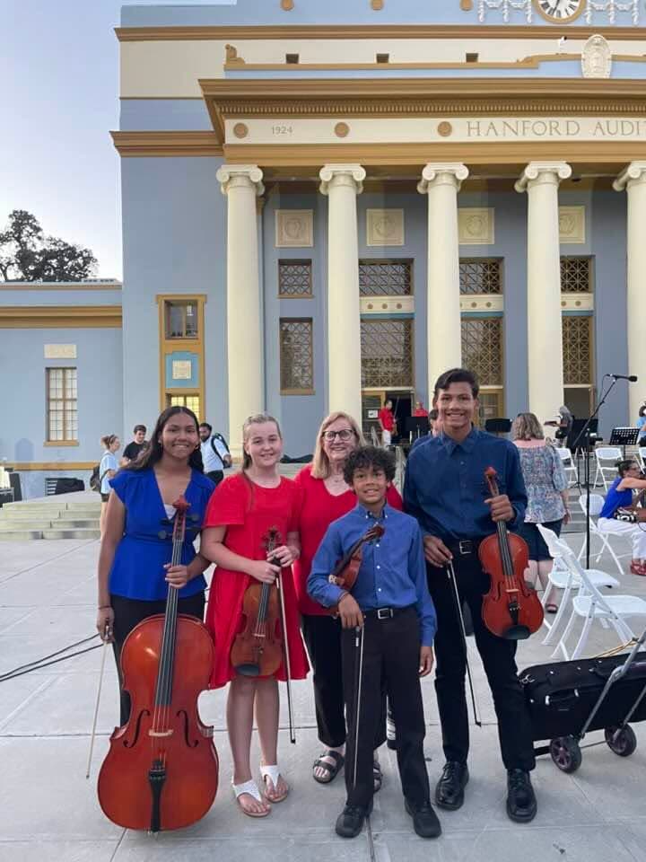 Four students with violins, a viola and a cello standing together before a performance.